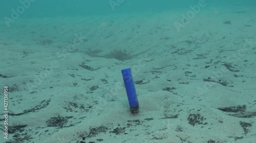 Underwater footage of a discarded cigarette lighter bobbing along the sea floor in the ocean current photo