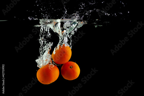 three tangerines fall into the water on a black background