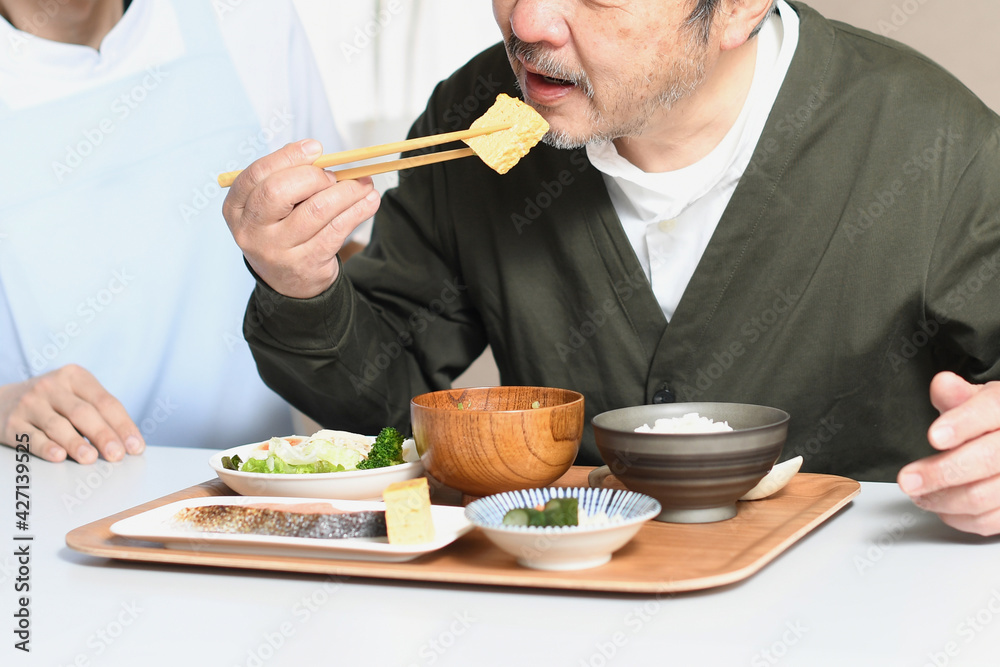 食事をする高齢者男性とエプロン姿の男性介護士 食事をする高齢者男性とエプロン姿の男性介護士