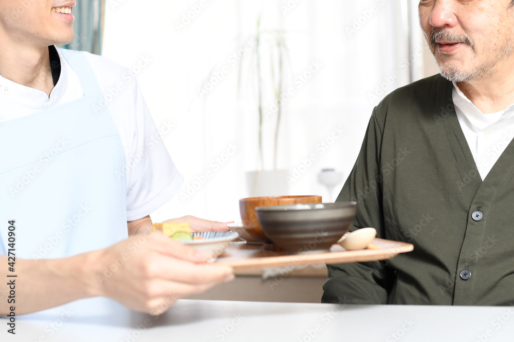 食事を運ぶ男性介護士と高齢者の白髪男性 食事を運ぶ男性介護士と高齢者の白髪男性