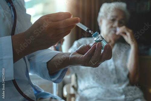 Doctor giving injection coronavirus vaccine to the elderly patient, general practitioner visiting her at home, elderly health care concept, selective focus