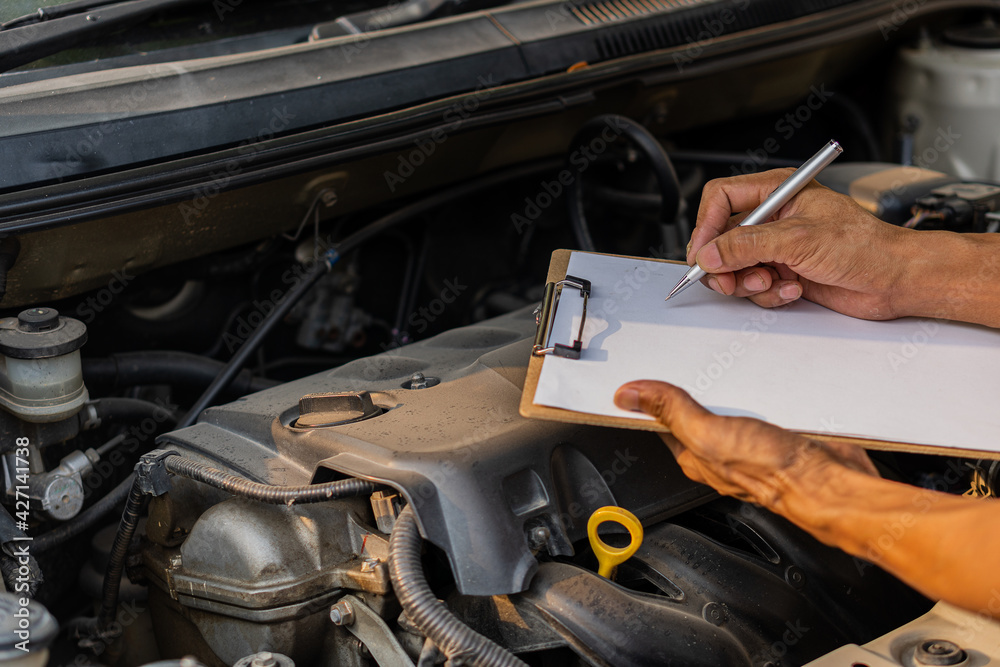 The auto mechanic checks the car engine with the check written in the car service engine repair checklist notebook. The auto mechanic checks the car engine with the check written in the car service engine repair checklist notebook.