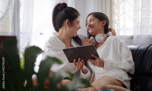 Cropped shot view beautiful young asian women LGBT lesbian happy couple sitting on sofa using laptop a computer and phone in living room at home. LGBT lesbian couple together.