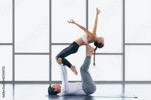 athletic couple practicing acro yoga or yoga partner together in gym