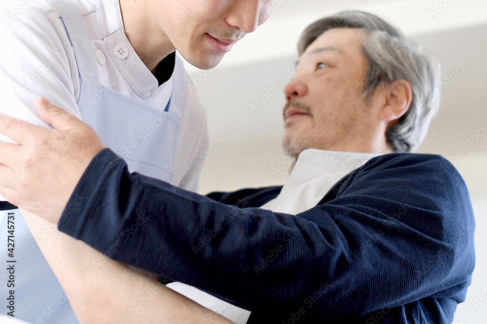 Obraz premium ベッドでお年寄りの男性を起こす介護士の男性