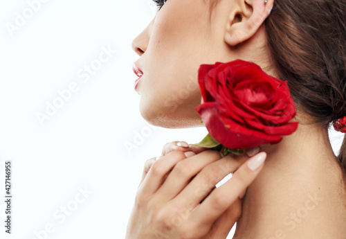Charming brunette woman holding red flower near her face and cropped view portrait
