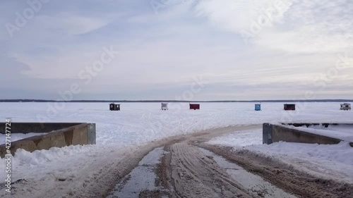 Flying over the marina ramp and unto the frozen lake showing some ice fishing huts and a beautiful sunset