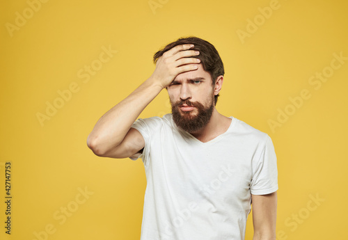 A man touches his face with his hands puzzled look yellow background cropped view