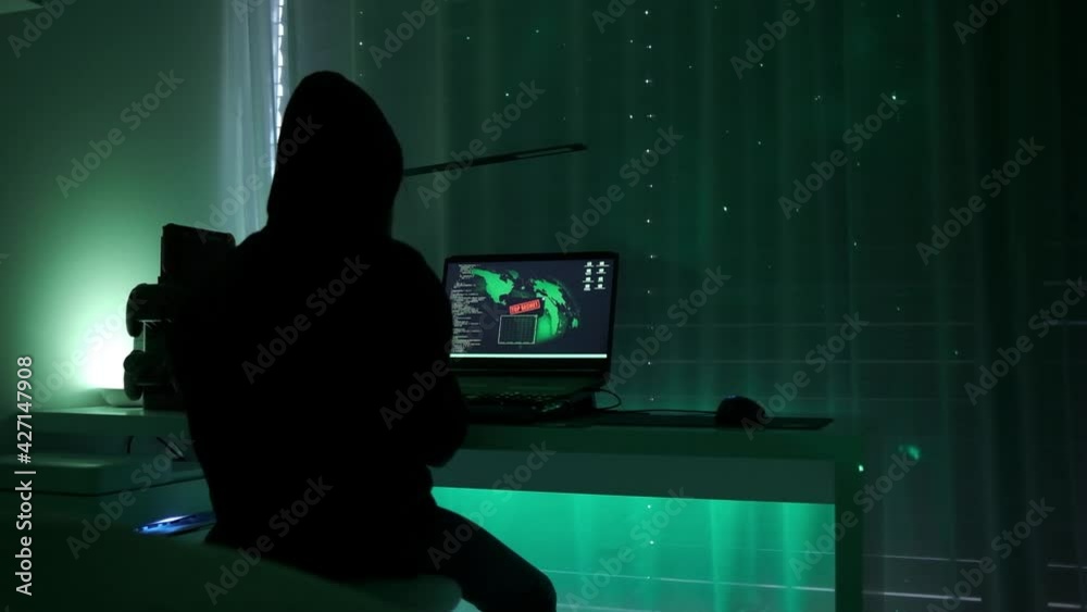 a criminal hackergirl with black hood using laptop and big computers to hack network system from her dark hacker neon room.