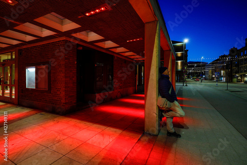 Halmstad, Sweden, A man on a street corner lit up at night in the color red.