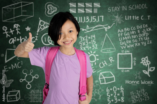 Adorable schoolgirl showing thumb up in classroom © Creativa Images