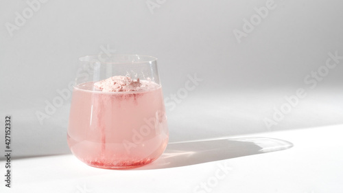 Super food. Glass of natural strawberry collagen protein powder in glass of water for skin regeneration. Trendy food additives. White background with sunlight and deep shadow of glass. Hard sunlight.
