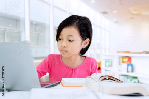 Cute little girl learning with book and laptop