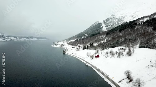 Aerial flyover Jolstravatnet Lake during cold foggy winter day beside overgrown mountains and empty road on shore. Skei,Norway. photo