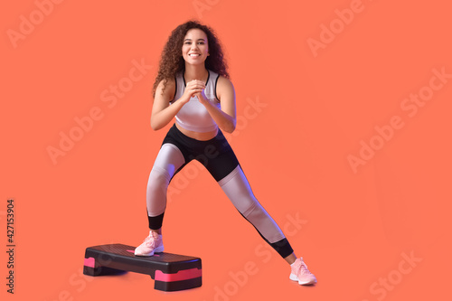 Beautiful young woman training with aerobic stepper on color background