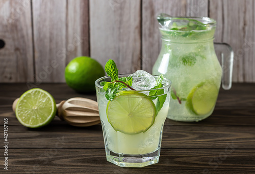 Homemade lemonade with lime, mint in a glass with a jug on a wooden rustic table. Summer refreshing drink.