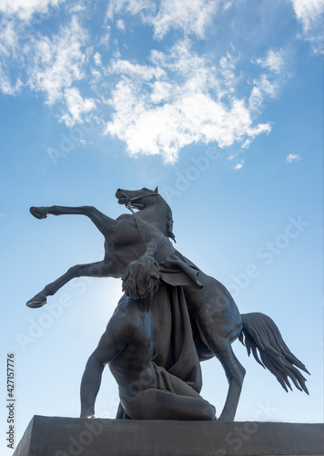 Bronze sculpture of athlete taming horse  at an Anichkov bridge in St. Petersburg against the blue sky.