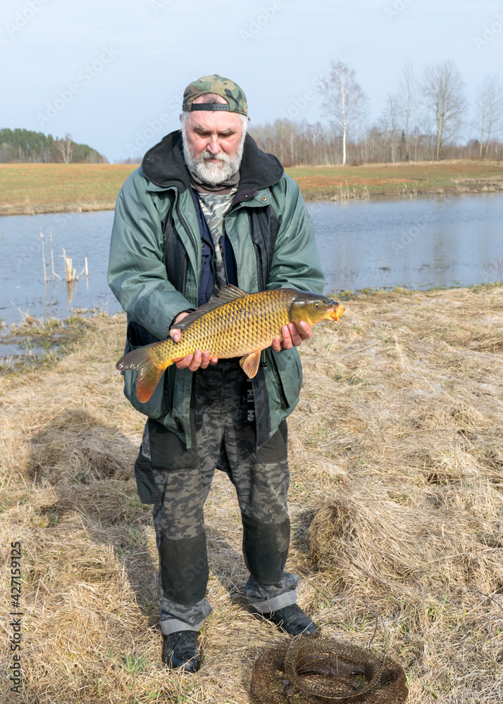 a fisherman on the shore of a lake, carp caught in the hands of a fisherman, amateur carp fishing, fishing as a hobby a fisherman on the shore of a lake, carp caught in the hands of a fisherman, amateur carp fishing, fishing as a hobby