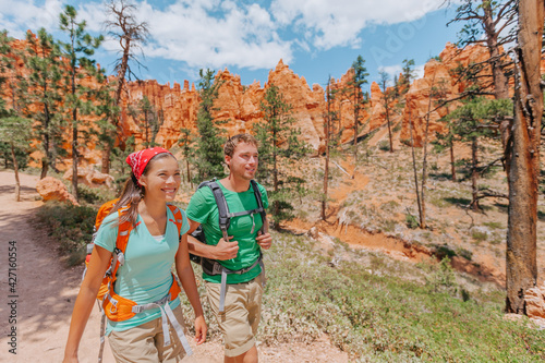 Hiking couple hikers walking smiling happy in summer mountain nature. Interracial couple Asian woman and Caucasian man in Bryce Canyon National Park landscape, Utah, United States.