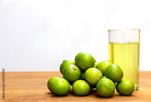 pile of green lemons on a rustic wooden table with a glass of lemon juice. Lemon has medicinal properties and vitamin C