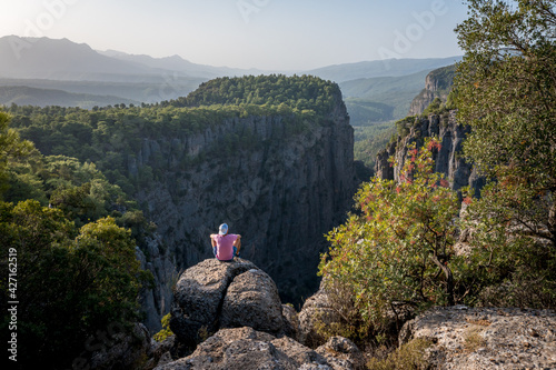 A man sits on the edge of a cliff against the backdrop of a gorge. The Tazi Canyon is located in the northern part of the Koprulu Canyon National Park, close to the cemetery of the Gaziler Village. photo