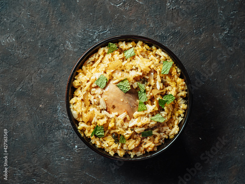 Pakistani food - biryani rice with chicken and raita yoghurt dip. Delicious hyberabadi chicken biryanion black textured background. Top view or flat lay