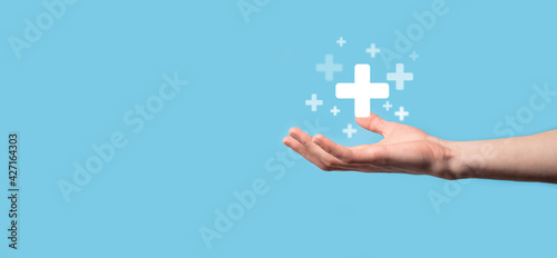 Male hand holding plus icon on blue background. Plus sign virtual means to offer positive thing like benefits, personal development, social network Profit,health insurance, growth concepts