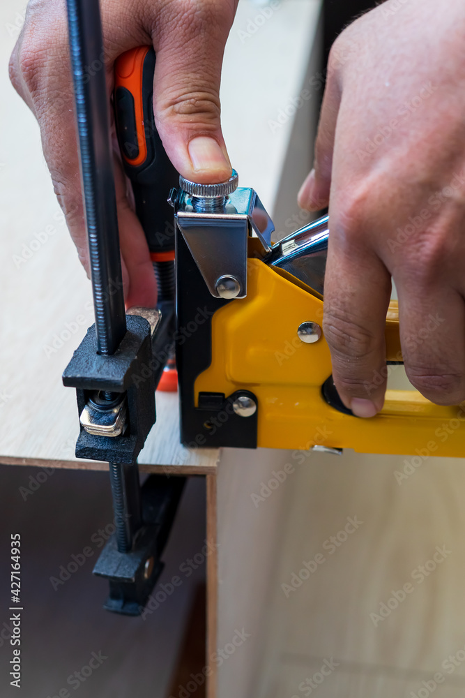 Carpenter using an industrial construction stapler on a wood plank.