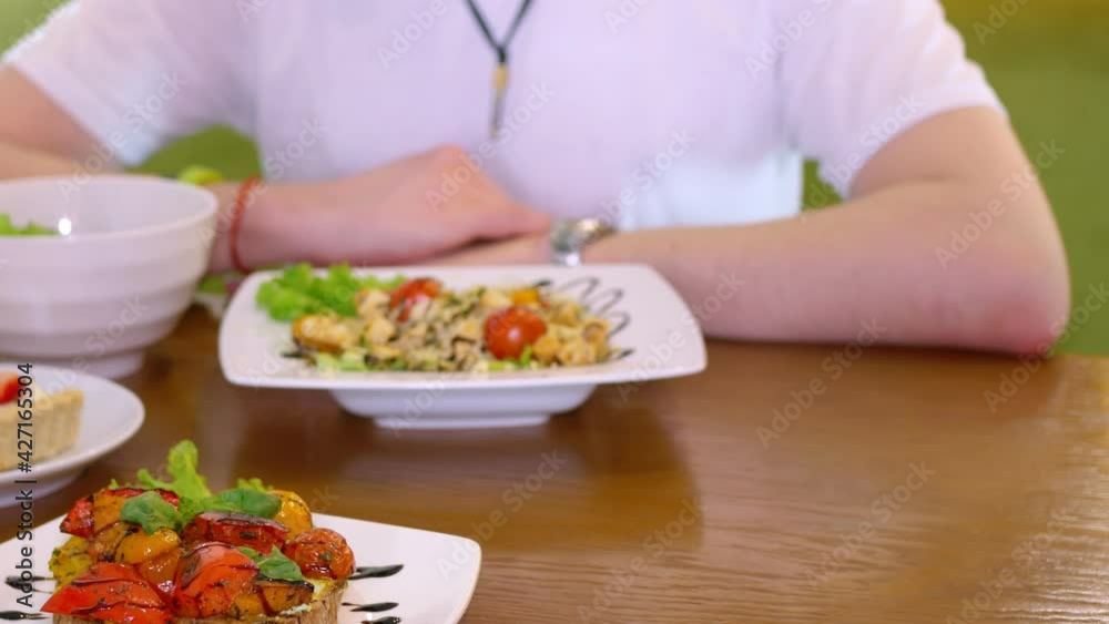 A guy and a girl are holding hands at a table in a restaurant. The waiter serves dishes on the table. On the table are plates with beautifully decorated dishes and dessert. Small business. Close-up.