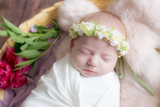 Baby girl in a wicker basket of vine decorated with burgundy peonies in a light winding and a flower wreath on her head. Spring photo. Flowers and children. Happy motherhood 
