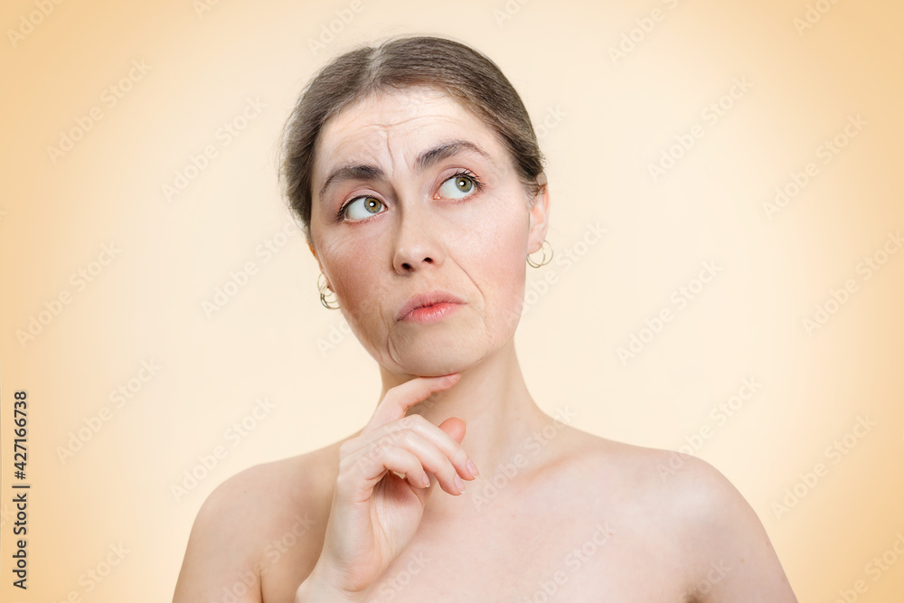 © _KUBE_ - Portrait of an elderly thoughtful woman on a beige background. Copy space. The concept of rejuvenation and plastic surgery