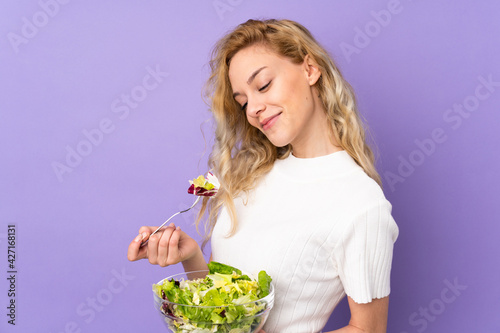 Tableau sur toile Young blonde woman holding salad isolated on purple background