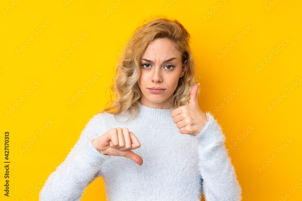 Young blonde woman isolated on yellow background making good-bad sign. Undecided between yes or not Young blonde woman isolated on yellow background making good-bad sign. Undecided between yes or not