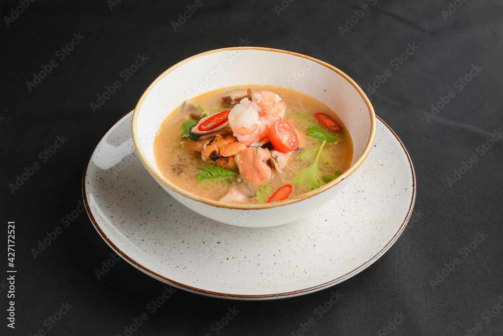 Broth soup with seafood. Shrimps and clams soup served in a white bowl over black background.