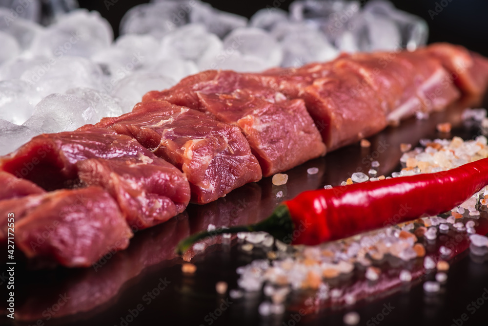 slicing for barbecue of fresh raw fresh meat on crushed ice with rosemary on a background of dark slate stone, top view. sloping horizon. Selective focus. Carnivores concept