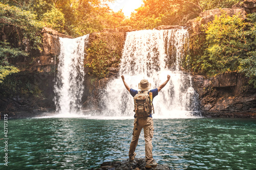 Fototapeta Naklejka Na Ścianę i Meble -  Happy man backpacker enjoying amazing tropical waterfall raised hands .
