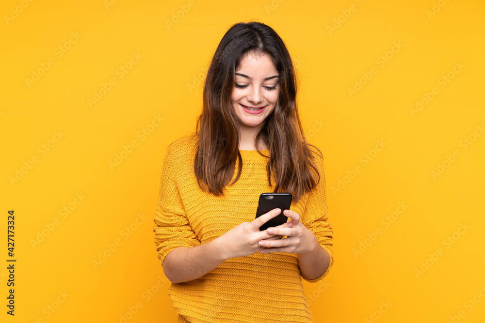 Young caucasian woman isolated on yellow background sending a message with the mobile Young caucasian woman isolated on yellow background sending a message with the mobile