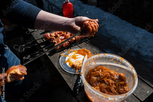 Barbecue in the backyard of your country house. A man's hand impales a piece of meat marinated in red sauce on a skewer. The process of cooking a delicious barbecue in nature. photo