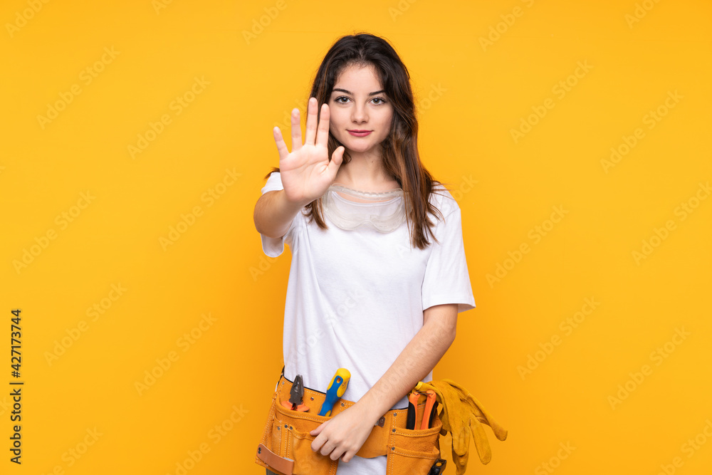 Young electrician woman over isolated on yellow background making stop gesture with her hand Young electrician woman over isolated on yellow background making stop gesture with her hand