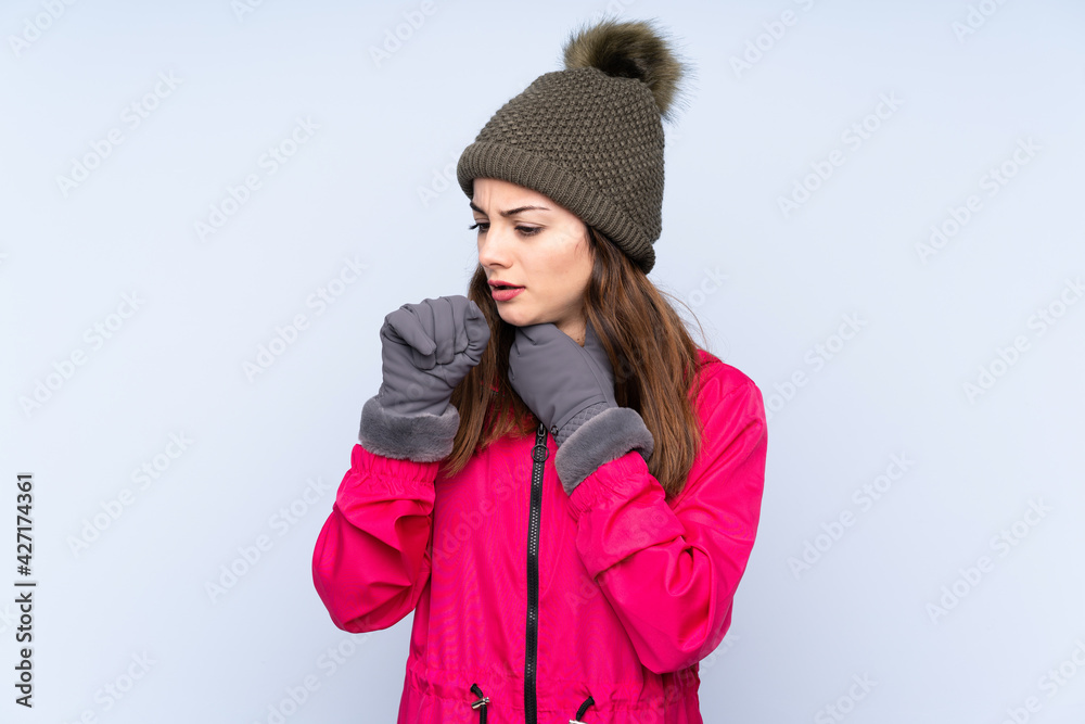 Young girl with winter hat isolated on blue background is suffering with cough and feeling bad Young girl with winter hat isolated on blue background is suffering with cough and feeling bad
