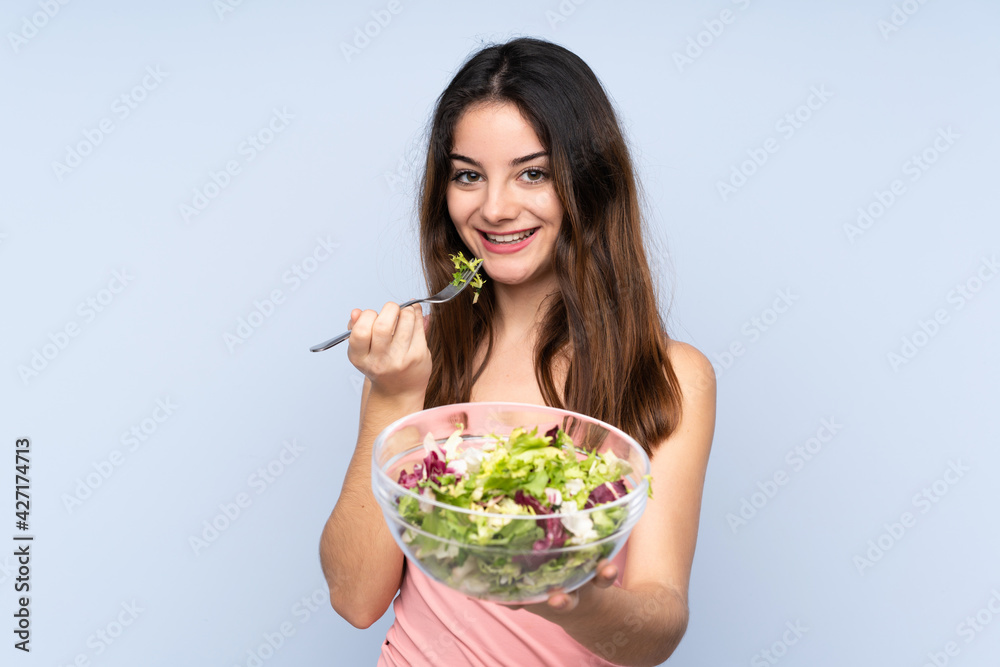 Young caucasian woman holding a salad isolated on blue background Young caucasian woman holding a salad isolated on blue background