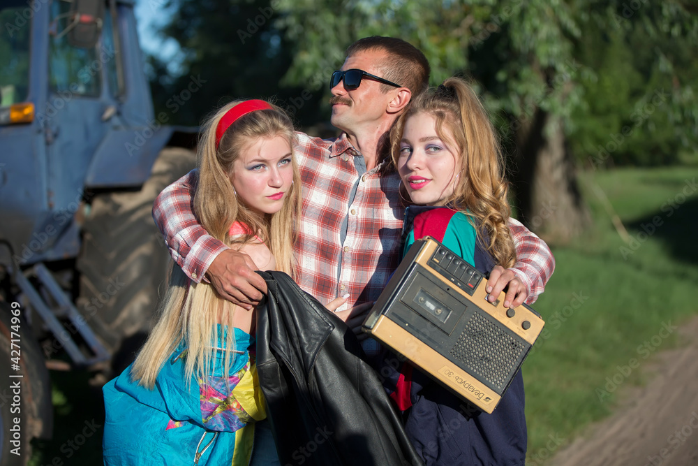 Obraz premium Funny man with cassette recorder hugs girls. People in the style of the nineties.