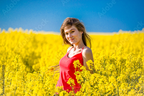 Portrait of a happy, smiling, woman standing in rapeseed field. Rural scene with model girl enjoying sun in yellow blooming farmland. Concept of joy, happiness and freedom.