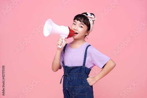 Happy Asian child girl shouting into megaphone making announcement in isolated on pink background.