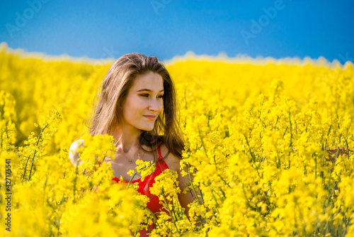 Beautiful, young woman in rapeseed field. Long hair, young smiling girl enjoying sun in blooming field.