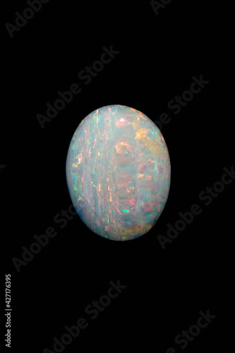 Photography Beautiful multi-coloured iridescent Australian white boulder opal gemstone cut in a cabochon shape with flashes of red, blue and green isolated on a black background