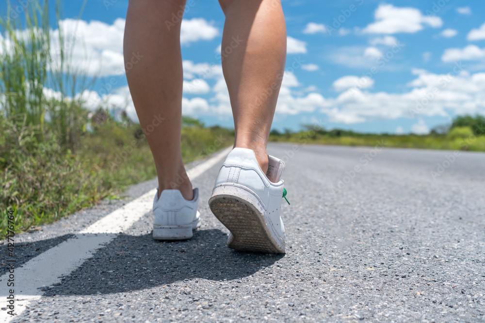 Woman is walking on small country road with blue sky background.