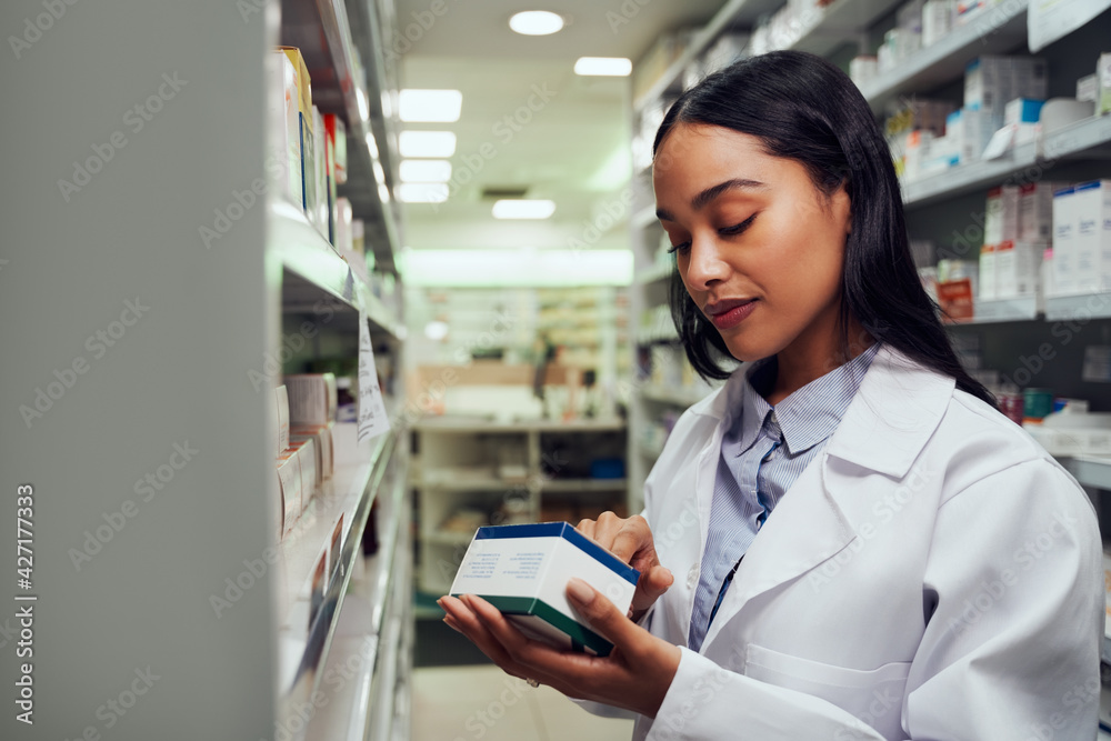 Young female pharmacist reading instructions on medicine box standing in aisle of chemist Young female pharmacist reading instructions on medicine box standing in aisle of chemist