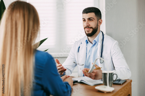 A serious male doctor of oriental appearance consults the patient, shows information about her illness and talks about the medical examination.
