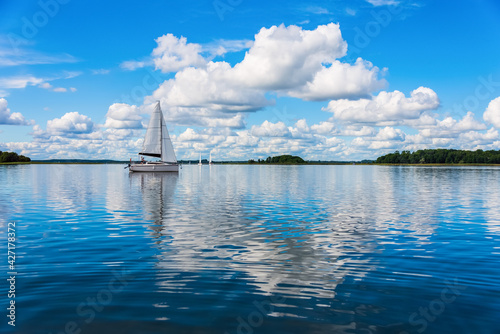 Fototapeta Naklejka Na Ścianę i Meble -  Sailing yacht in the lake with gloomy sky before the rain. Yacht sailing on the lake against a blue sky with clouds. Sailboat vacations on a lake.